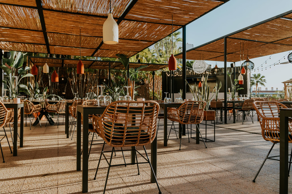 Terraza de restaurante al aire libre en Tenerife con sillas de mimbre y plantas.