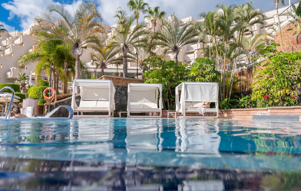 Piscina y camas balinesas rodeadas de palmeras en un hotel en Tenerife.