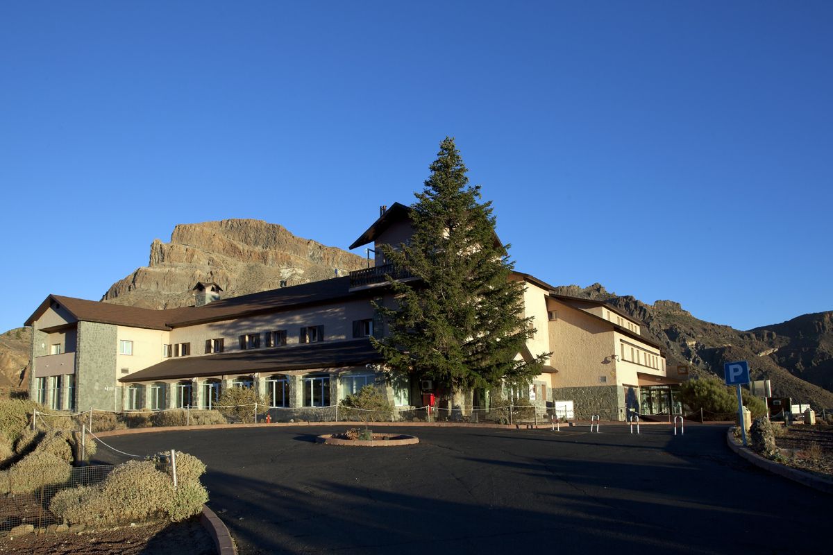 Edificio ladeado por árboles, montañas al fondo en Tenerife.