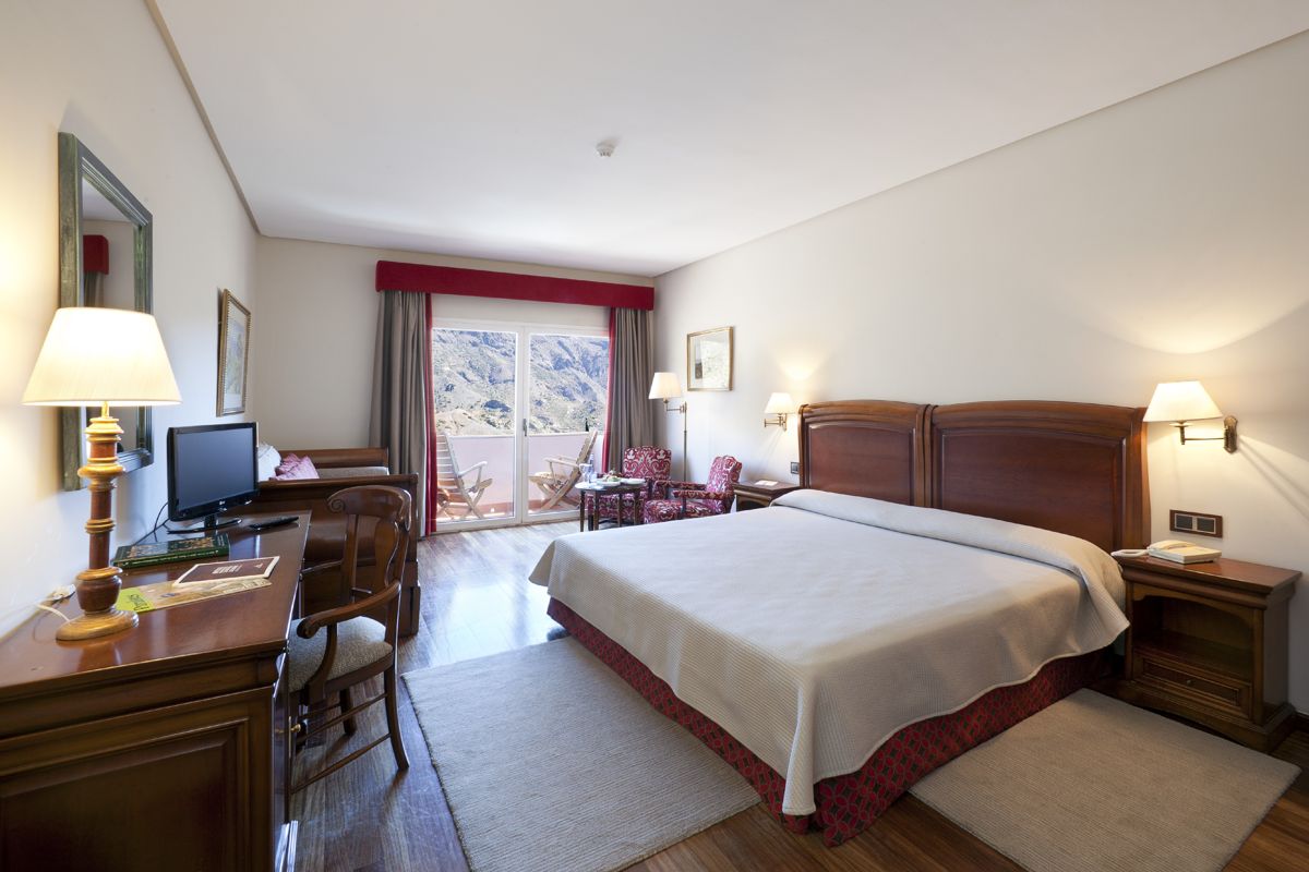 Habitación de hotel con cama doble, televisor y balcón con vista a montañas en Tenerife.