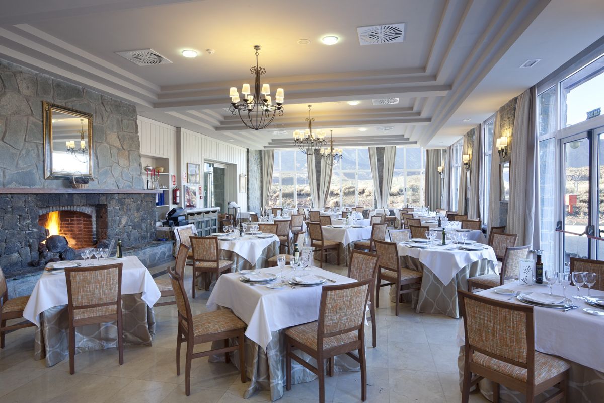 Restaurante con ventana panorámica y chimenea en Tenerife, mesas cubiertas de manteles blancos.