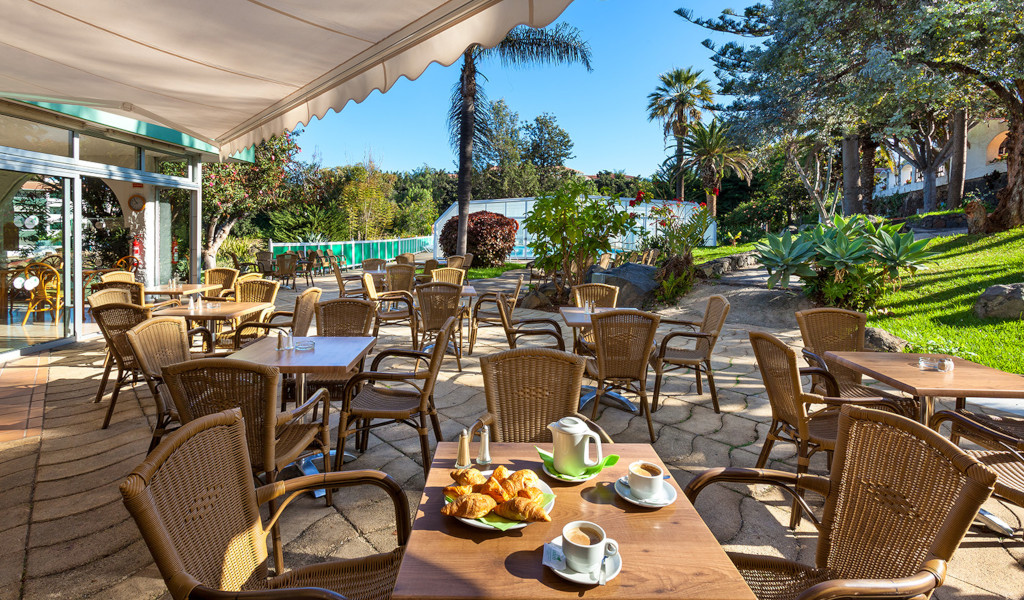 Terraza con mesas y sillas en un jardín de Tenerife, croissants y café sobre la mesa.