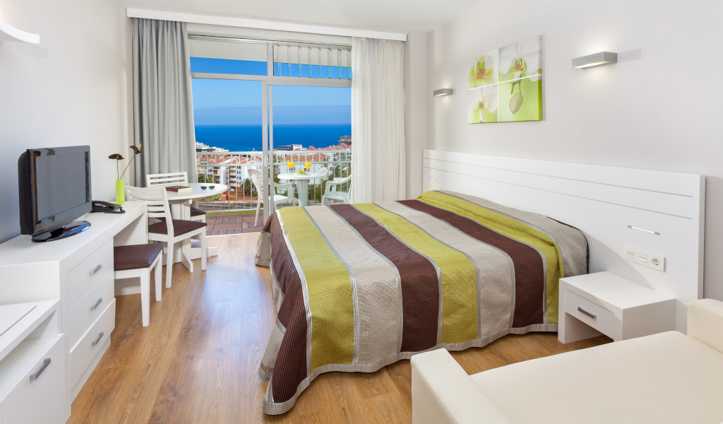 Habitación con cama doble, mesa redonda, televisor y vista al mar en Tenerife.