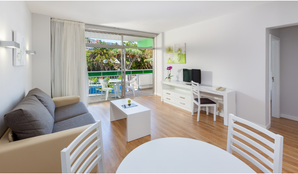 Sala de estar con sofá, mesa y TV, vista al jardín en Tenerife.