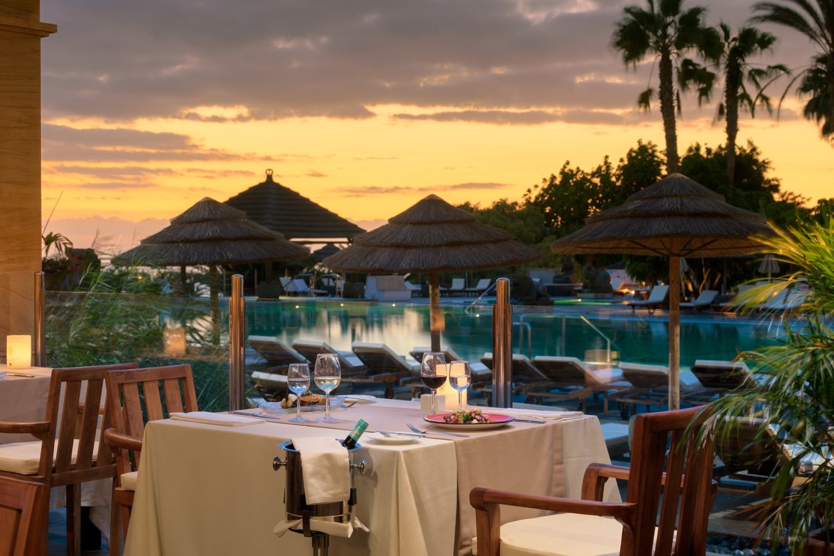 Mesa frente a piscina al atardecer en restaurante de Tenerife con palmeras.