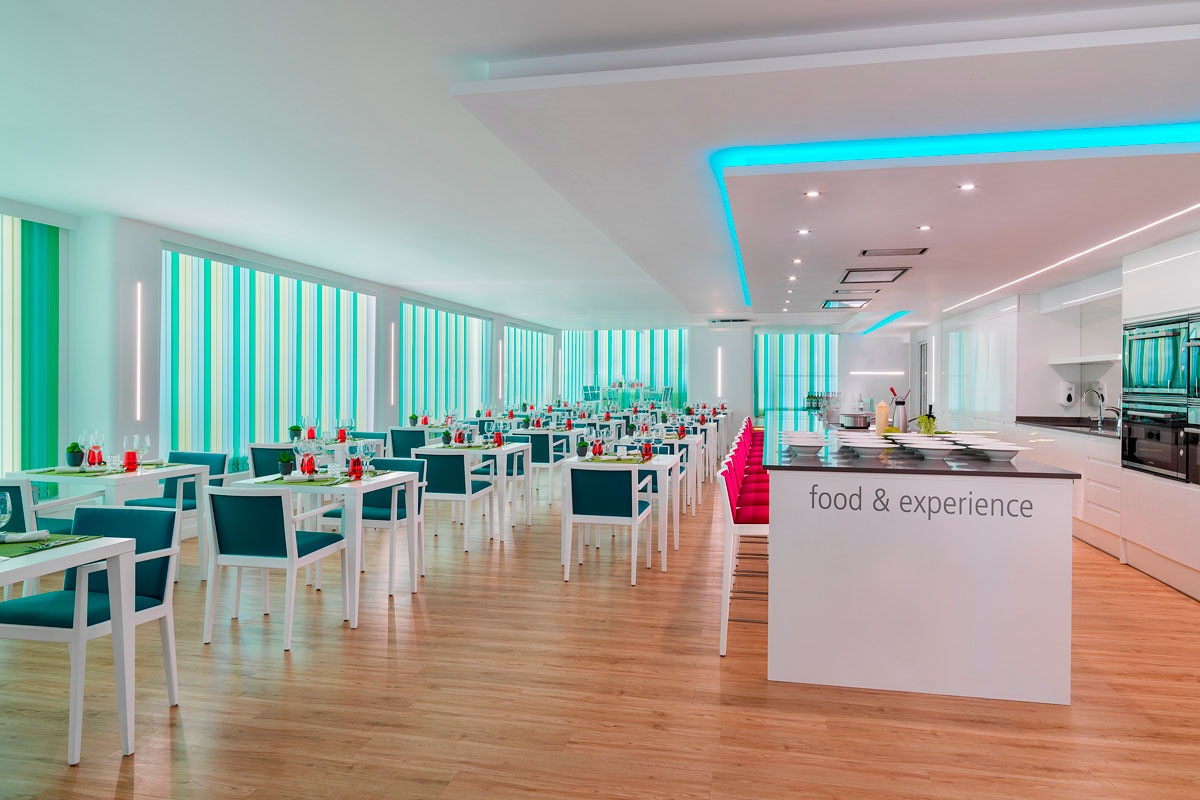 Restaurante iluminado con sillas azules y rosas, mesa central con food & experience.