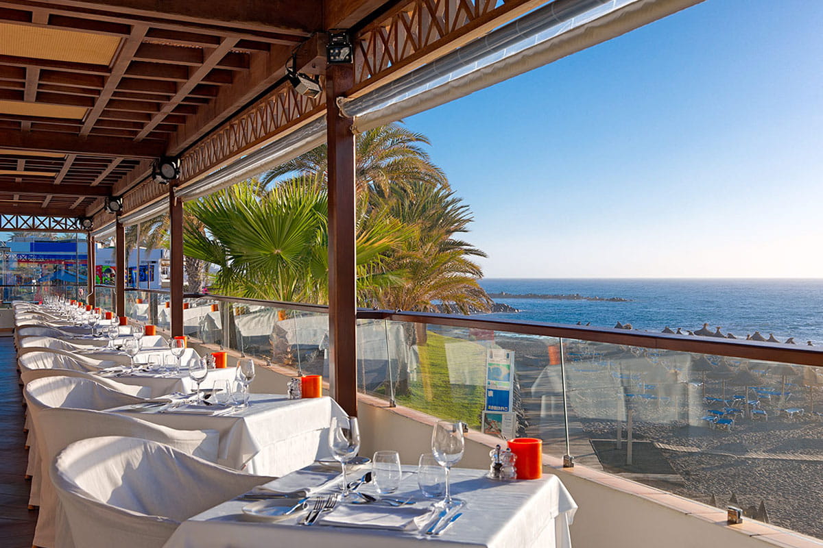 Terraza de restaurante con vista al mar en Tenerife, mesas preparadas para comensales.