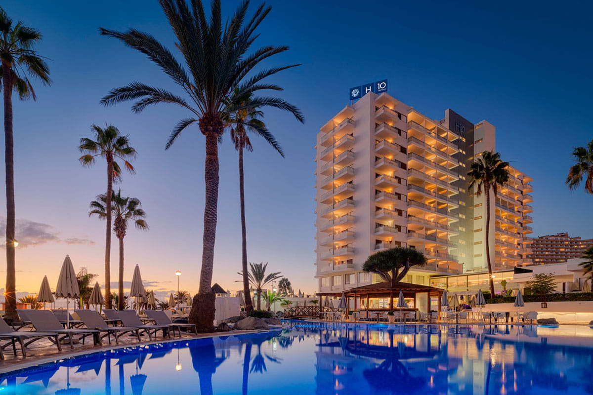 Hotel con piscina al atardecer en Tenerife, rodeado de palmeras y tumbonas.