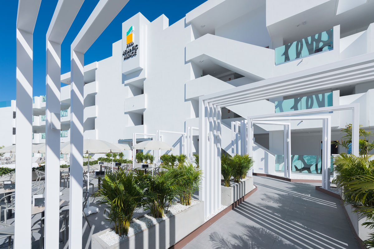 Entrada moderna al hotel Atlantic Mirage en Tenerife, con plantas y sombrillas.