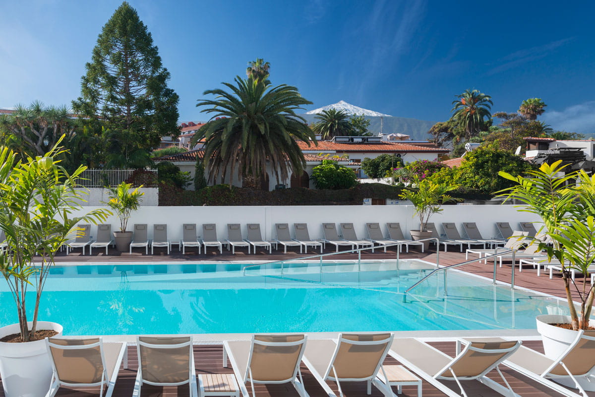 Piscina al aire libre en Tenerife con sillas y palmeras alrededor.
