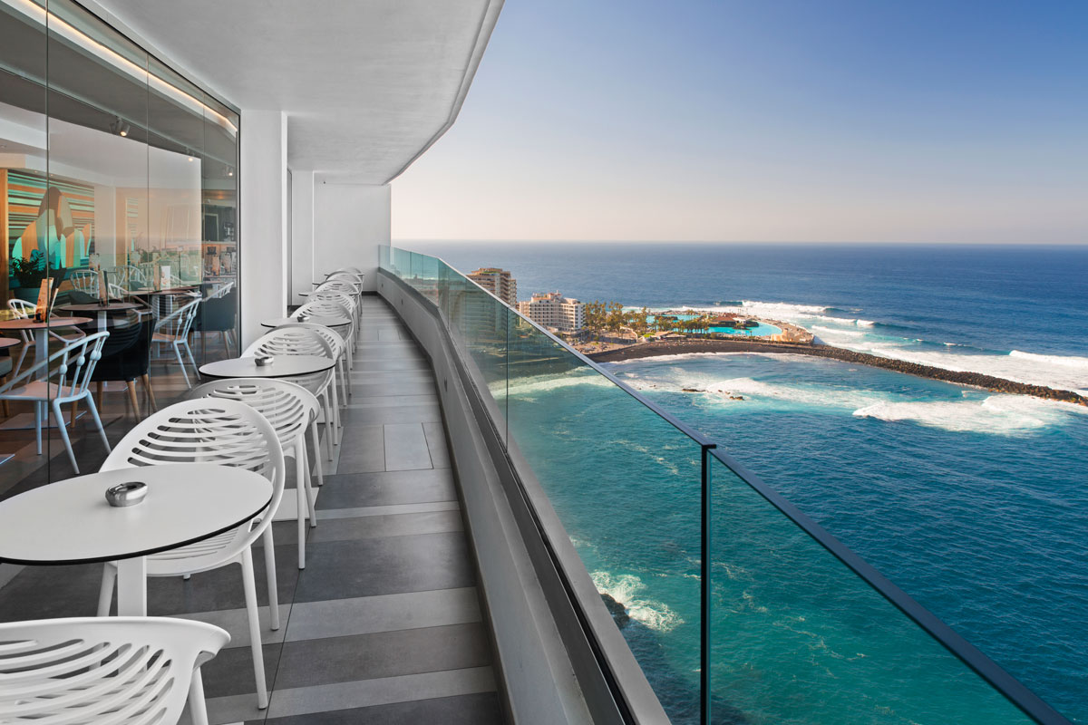 Terraza con vista al océano en Puerto de la Cruz, Tenerife. Mesas y sillas alineadas.