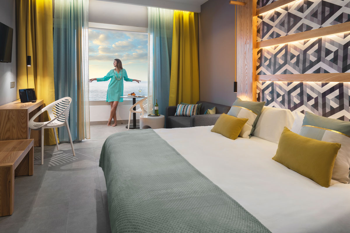 Habitación moderna en Tenerife con vista al mar, mujer de pie junto a la ventana.