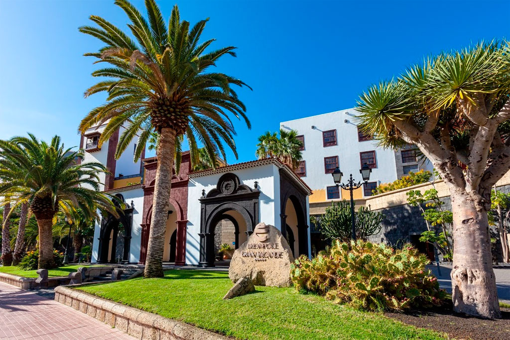 Edificio con palmeras y cactus en Garachico, Tenerife. Texto en roca: Convento San Francisco.
