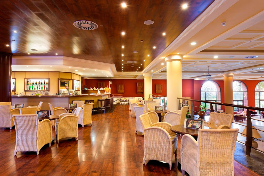Salón de un hotel en Tenerife con mesas, sillas de mimbre y una barra iluminada.