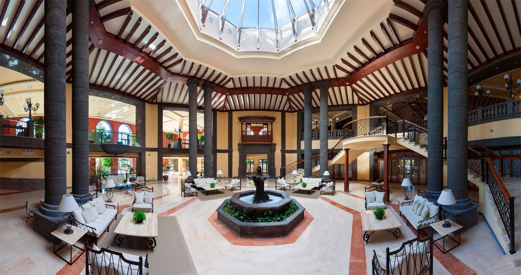Vestíbulo del hotel con techo de cristal en Tenerife, decoración elegante y columnas altas.