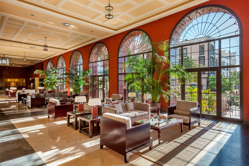 Sala con sofás, mesas y grandes ventanas arqueadas en hotel de Tenerife.