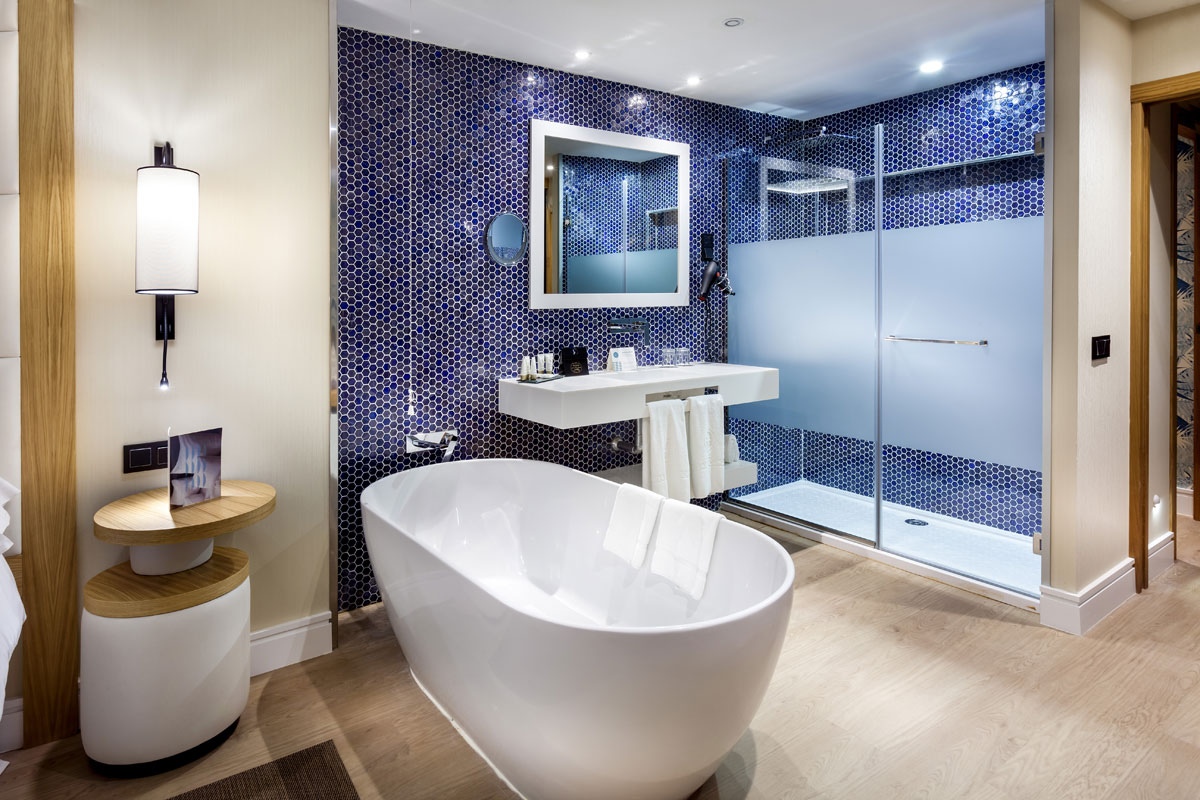 Baño moderno con bañera blanca y ducha, azulejos azules en Tenerife.