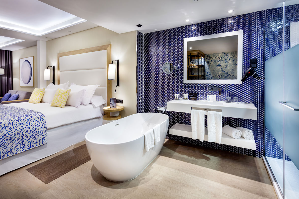 Baño moderno con bañera blanca y paredes azul mosaico en Tenerife.