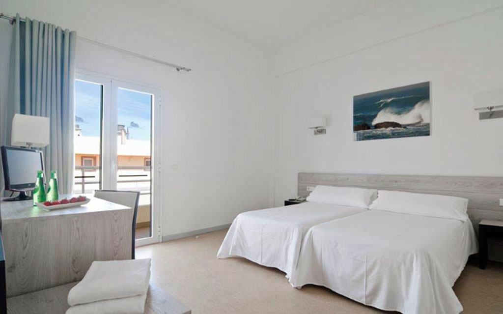 Habitación de hotel en Tenerife con dos camas, escritorio y terraza.