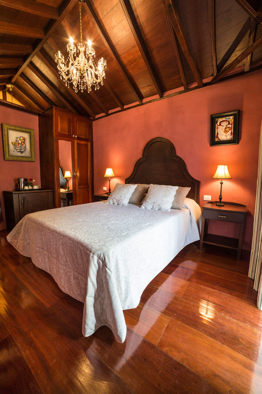 Habitación con cama doble, techo de madera y lámpara de araña en Tenerife.