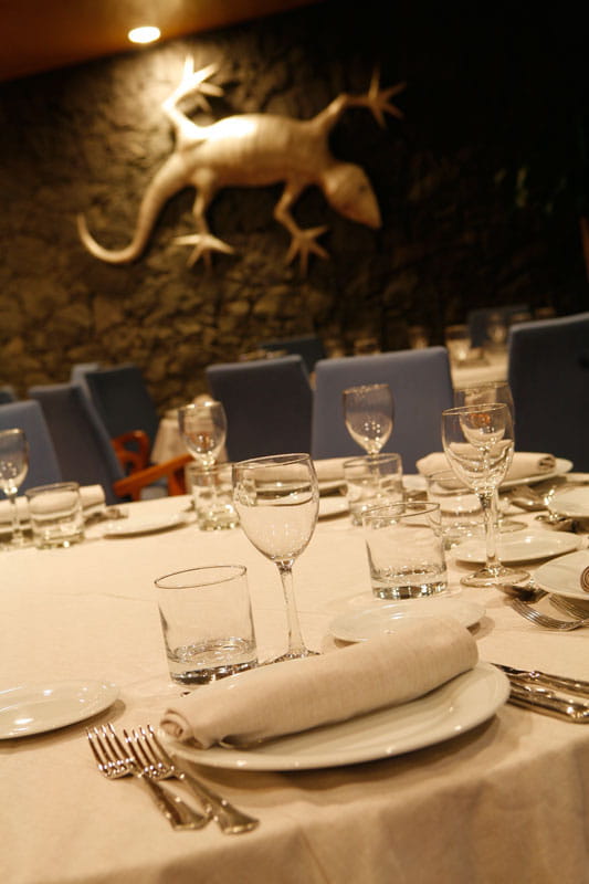 Mesa de restaurante en Tenerife con cubiertos y copas elegantes. Estatua de lagarto en la pared.
