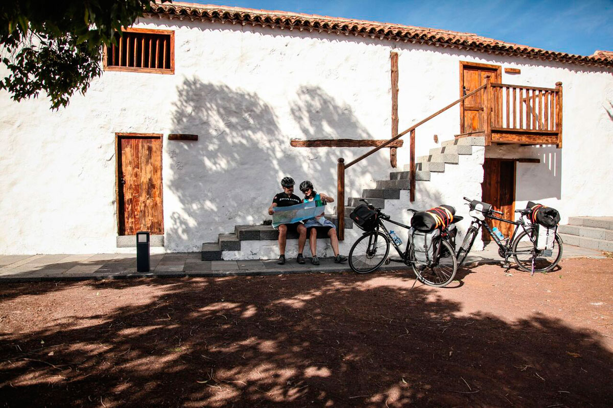 Ciclistas consultando un mapa junto a dos bicicletas frente a una casa en Tenerife.