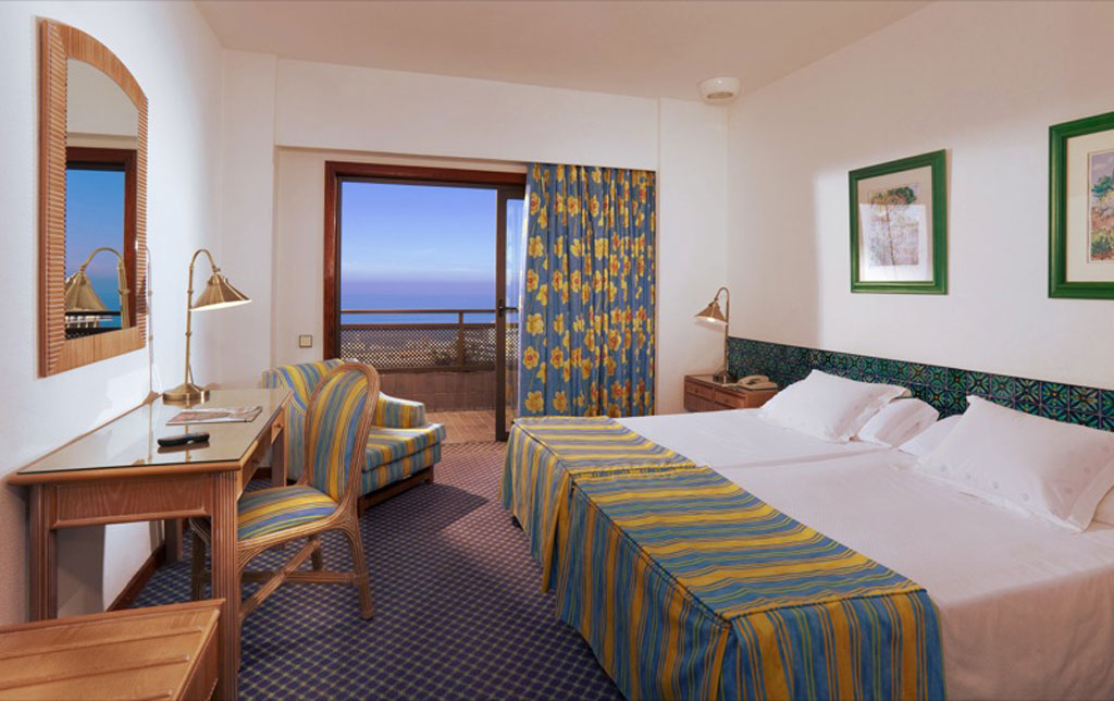 Habitación de hotel en Tenerife con dos camas, escritorio y vista al mar.