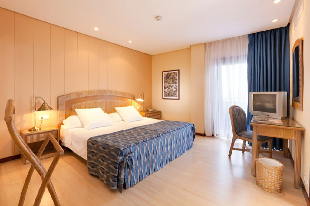 Habitación de hotel con cama doble, mesita, lámpara y televisor en Tenerife.