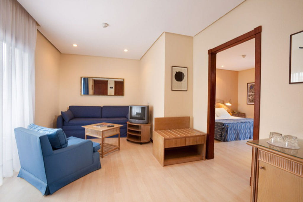 Sala de estar con sofá azul, televisión y vista al dormitorio en hotel de Tenerife.