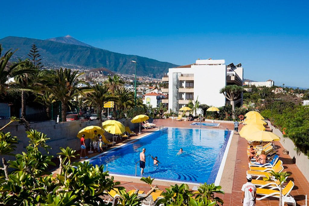 Piscina con sombrillas amarillas y vista del Teide en Puerto de la Cruz, Tenerife.