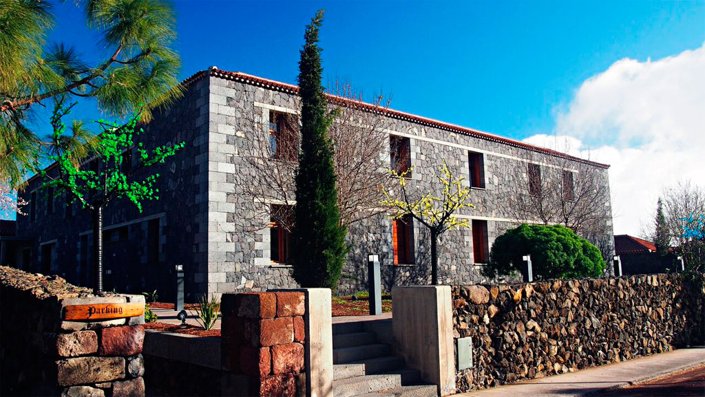 Antiguo edificio de piedra rodeado de árboles y muro, cartel: Parking, en Tenerife.
