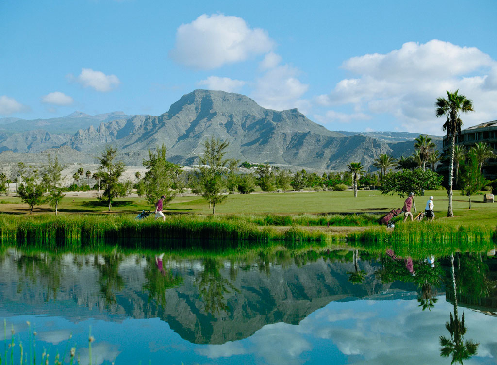 Campo de golf en Tenerife con montañas de fondo y reflejo en lago.