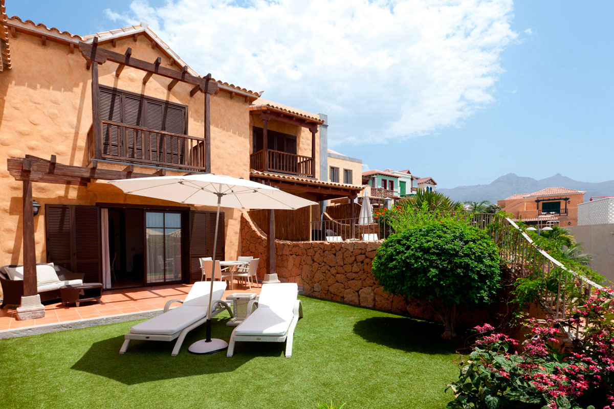 Casa con jardín en Tenerife, tumbonas, sombrilla y plantas en primer plano, cielo despejado.