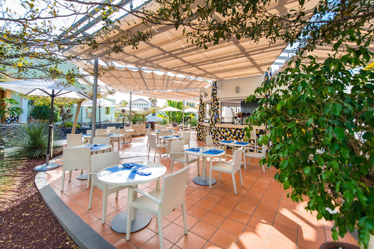 Terraza de un restaurante en Tenerife con mesas y sillas blancas bajo un toldo.