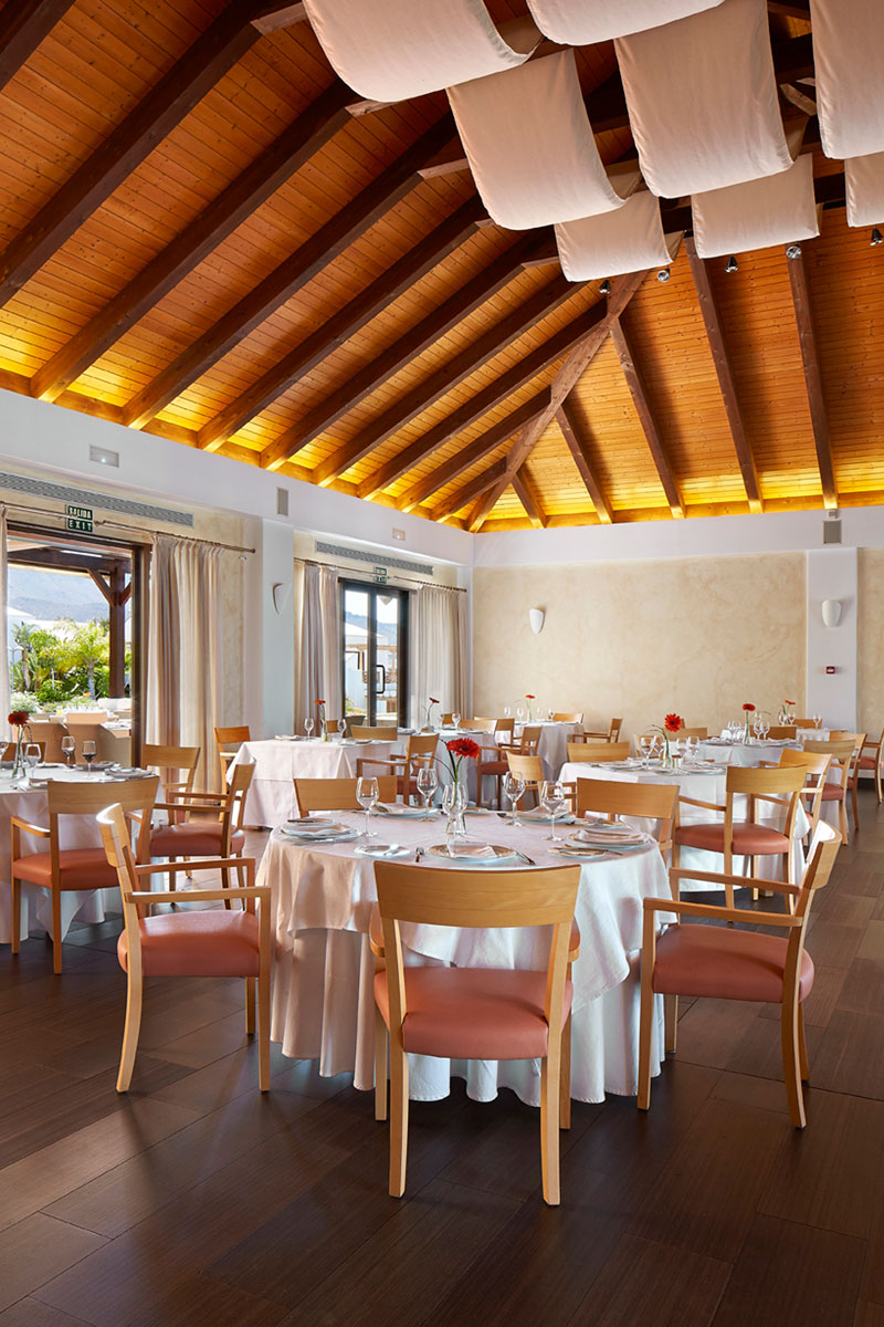 Restaurante con techo de madera y mesas vestidas en Tenerife, salida de emergencia visible.
