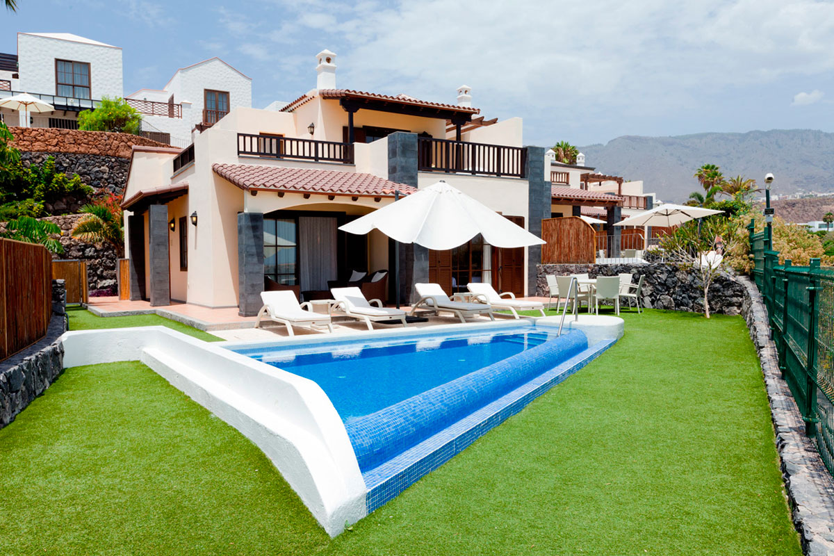 Casa con piscina y sillas de playa en Tenerife, rodeada de césped y montañas al fondo.