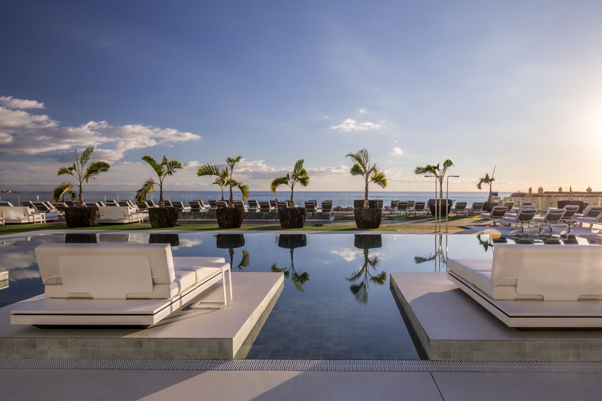 Piscina infinita con tumbonas y palmeras frente al mar en Tenerife.