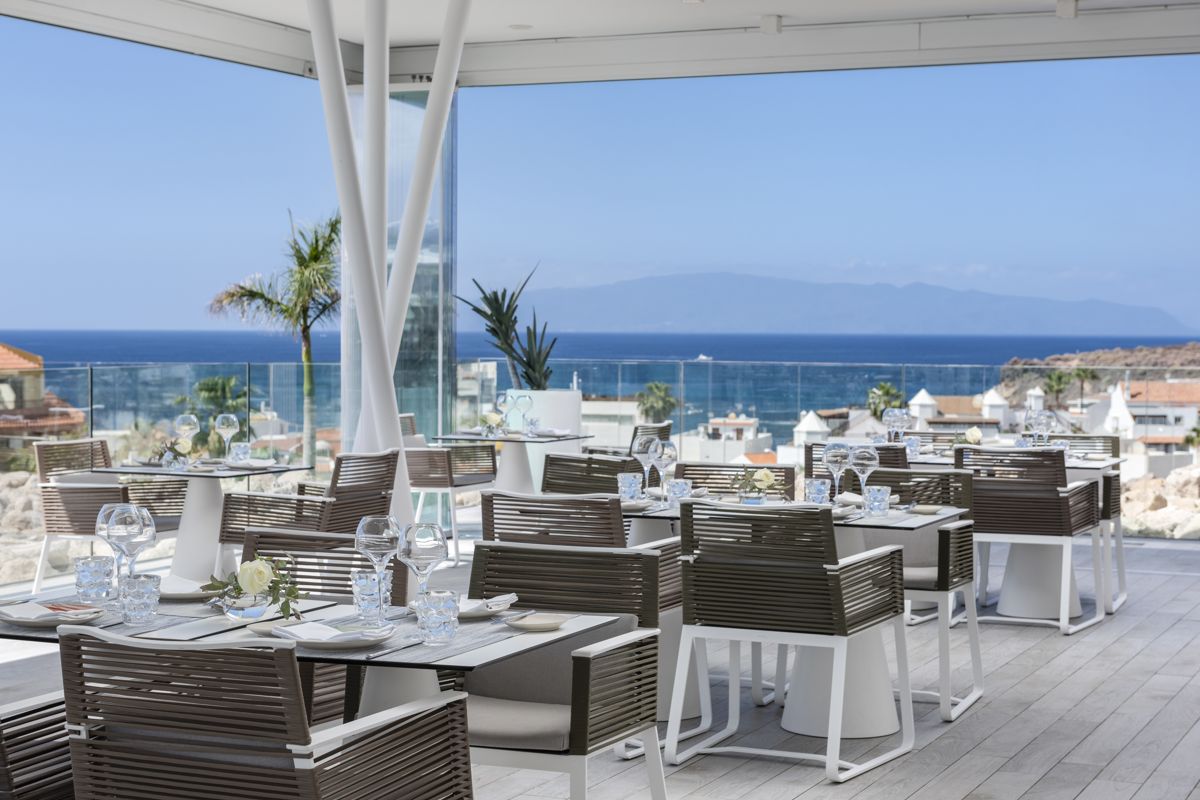 Terraza de restaurante con vista al mar en Tenerife, mesas preparadas para servicio.