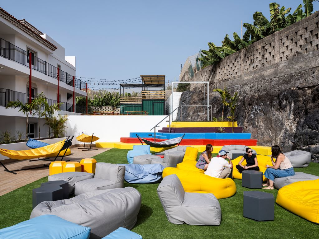 Personas conversan en espacio exterior con hamacas y puffs coloridos en Tenerife.