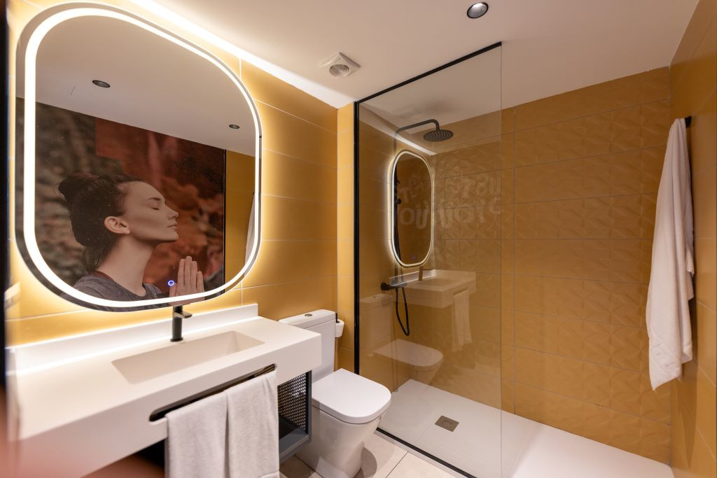 Baño con ducha, lavabo, espejo iluminado y fotografía de mujer meditando en Tenerife.