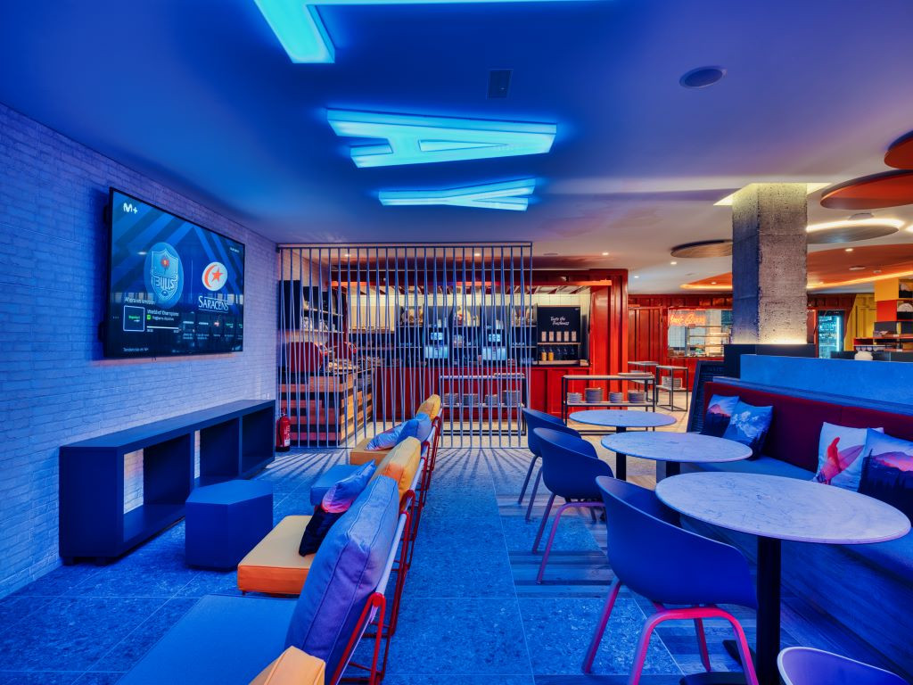 Zona de descanso iluminada en bar de Tenerife con pantalla y mesas.