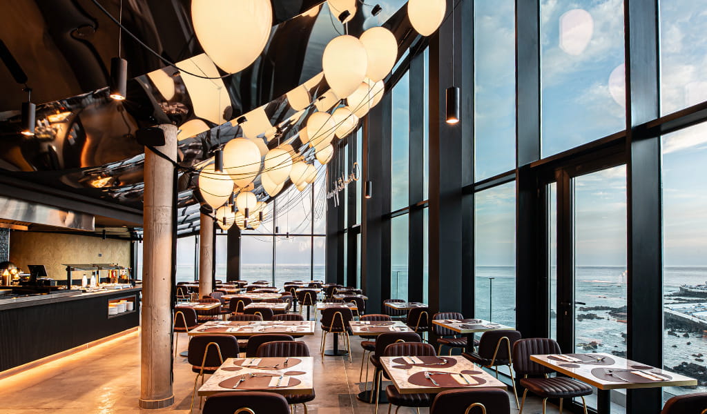 Restaurante con vista al mar en Tenerife, mesas preparadas bajo lámparas esféricas.