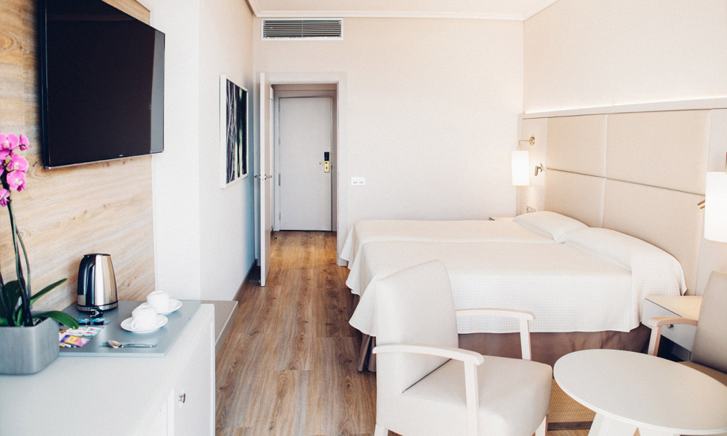 Habitación de hotel en Tenerife con camas gemelas, mesa, sillas y televisor en la pared.