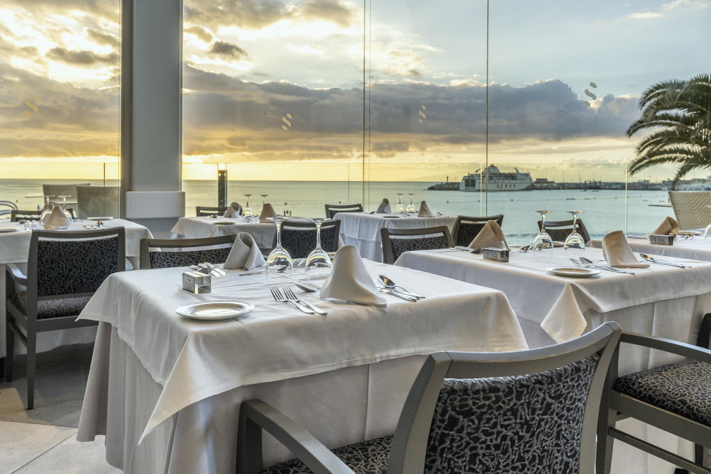 Mesas arregladas en un restaurante con vista al mar y el puerto en Tenerife al atardecer.
