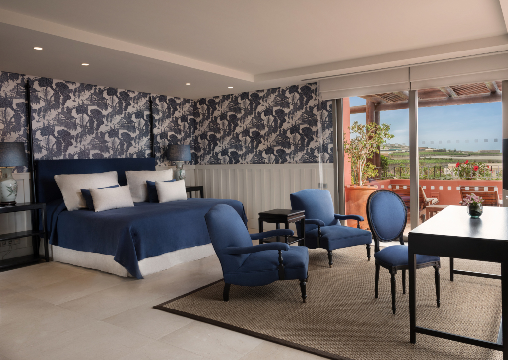 Habitación de hotel en Tenerife con cama, sillones azules y terraza con vistas al exterior.