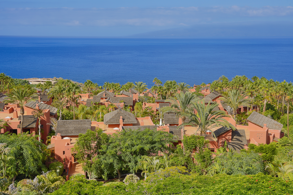 Complejo de casas con techos de paja y vegetación frente al mar en Tenerife.