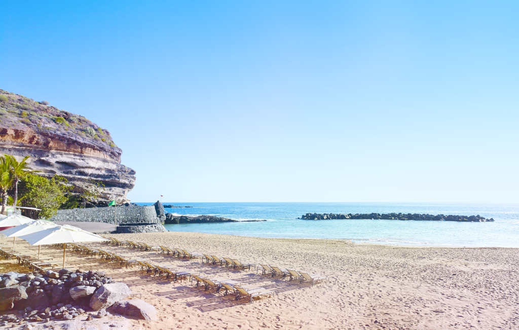 Playa con sombrillas y tumbonas en Tenerife. Mar y acantilado a la izquierda.