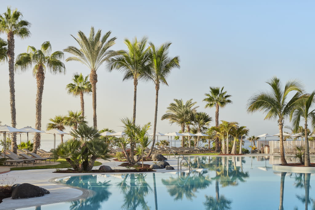 Piscina rodeada de palmeras en un hotel de Tenerife con cielo despejado.
