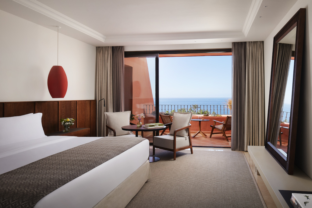 Habitación de hotel con vistas al mar en Tenerife, cama grande y balcón con mesas y sillas.