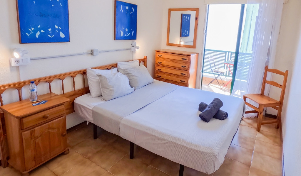 Dormitorio en Tenerife con cama, mesita, cajonera y balcón.